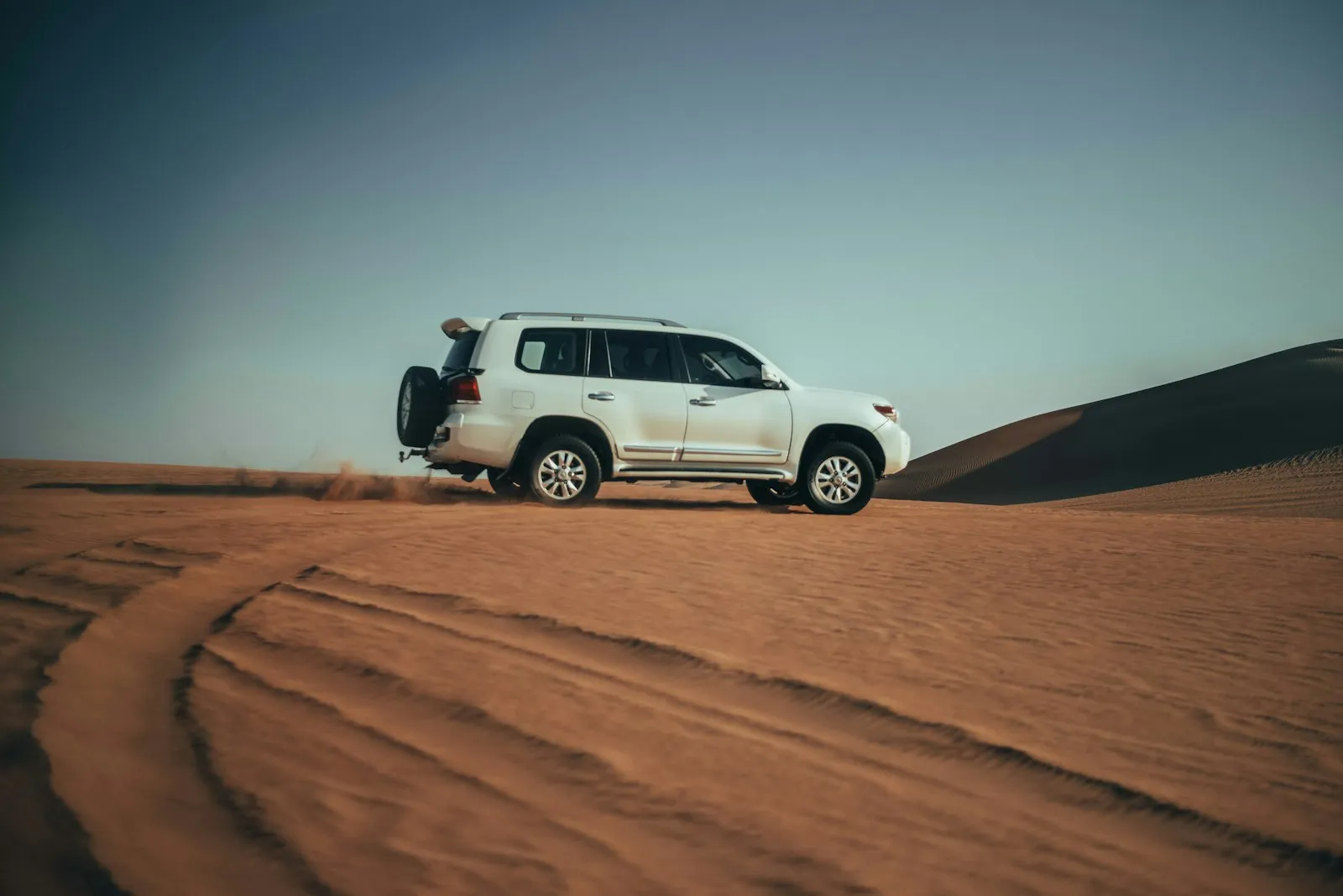 砂丘の上を走る白い SUV。GCC 仕様の車が使われる湾岸の環境